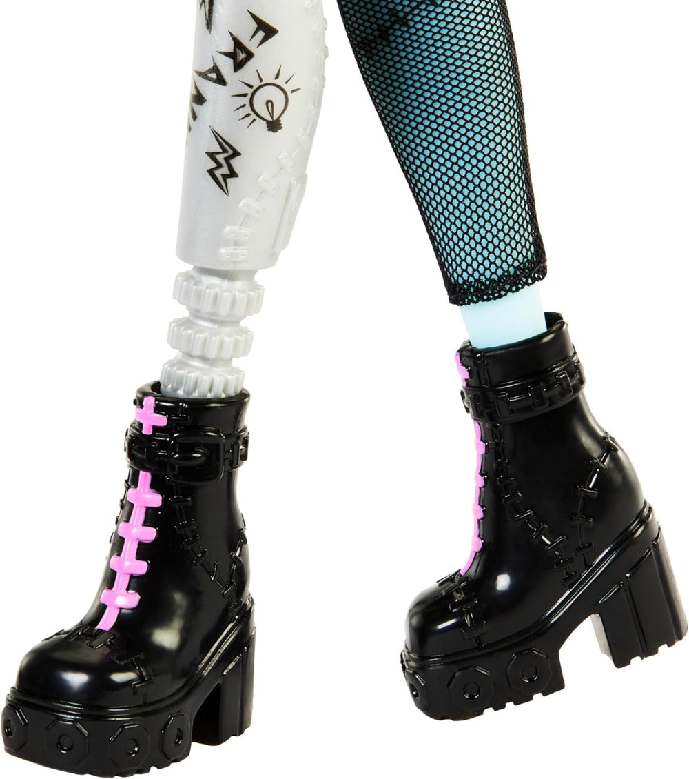 Păpușa Monster High Frankie Stein în jachetă de blugi și pantaloni scurți, include și cățelușa ei Watzie și accesorii precum un rucsac, o gustare și un caiet, HXH73
